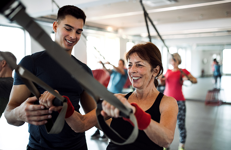 Lady at a gym smiling next to her personal trainer