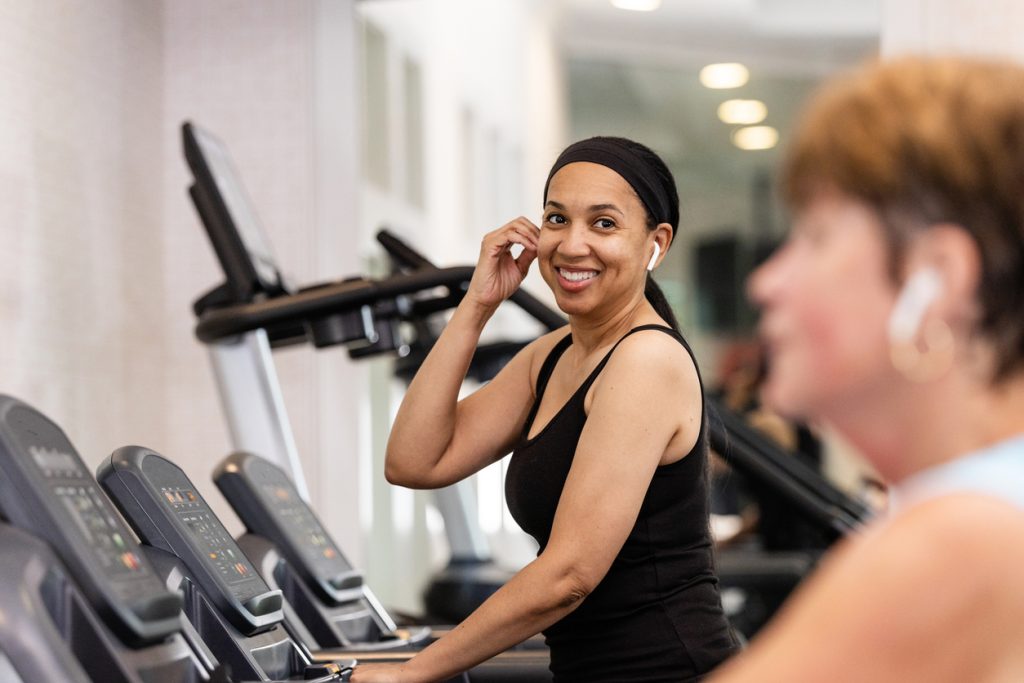 While walking on the treadmill, the mid adult female checks on another female who is next to her.