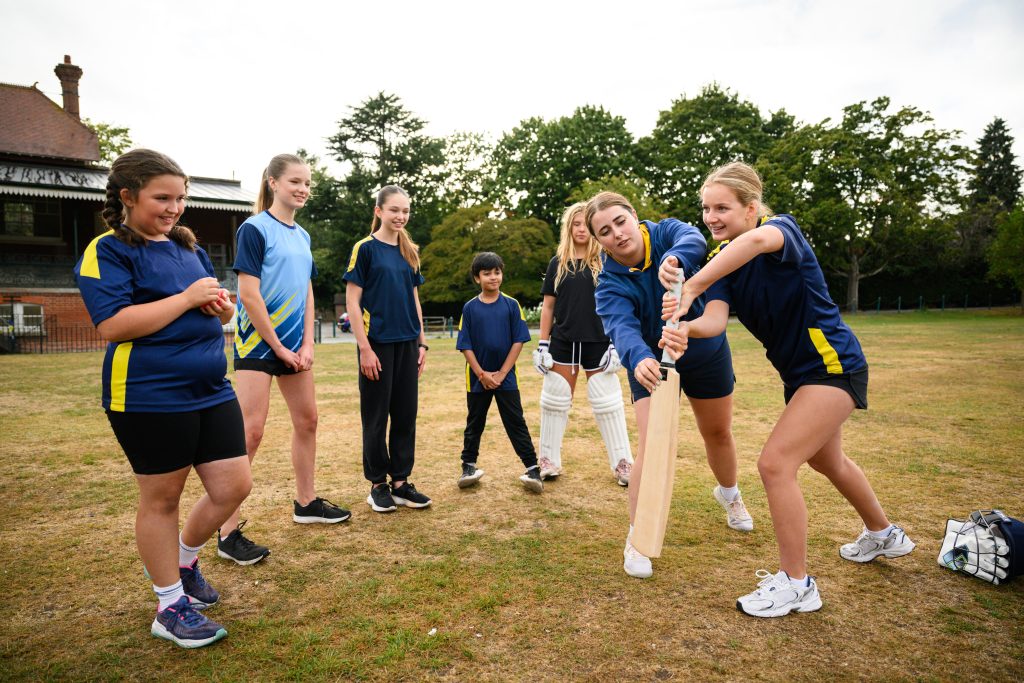 A young women teaches a group of girls how to hold a cricket bat