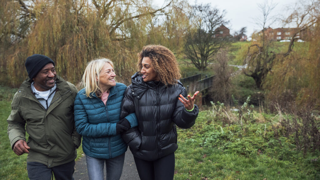 A senior multi-ethnic couple and their mixed race daughter wearing casual winter clothing and walking through their local park.