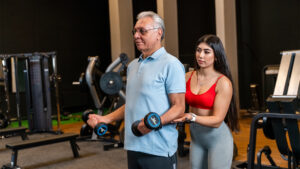 senior male lifting weight with a assistance of his coach
