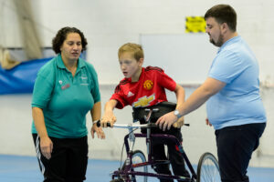 Disabled child on tricycle being supported by two volunteer coaches