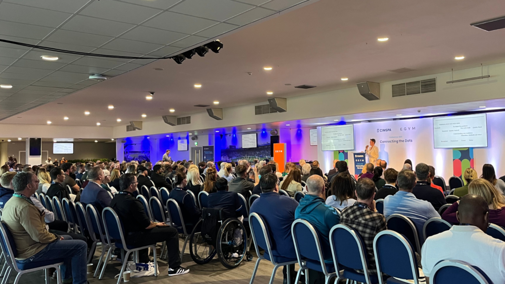 Tara Dillon delivers a speech in front of a crowded audience at the CIMSPA conference 2025.