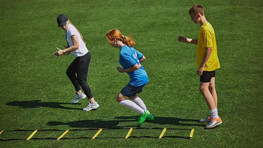 Athletic Training on Field Kids wearing sports gear engaged in challenging footwork exercise with agility ladder equipment.